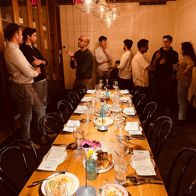 Several people gathered around an elegantly set long dining table in a restaurant private dining room with warm lighting.